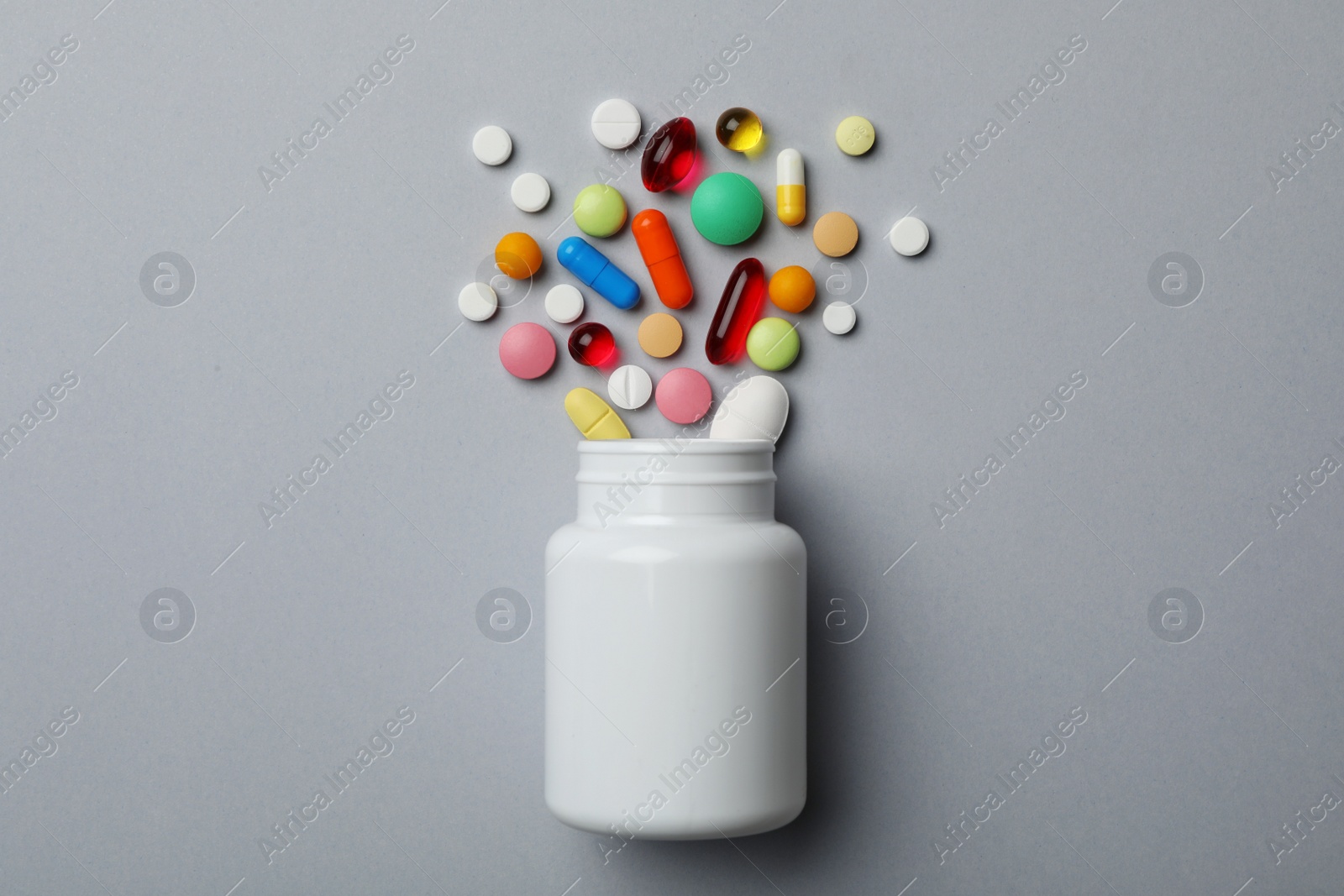 Photo of Bottle with different pills on grey background, flat lay