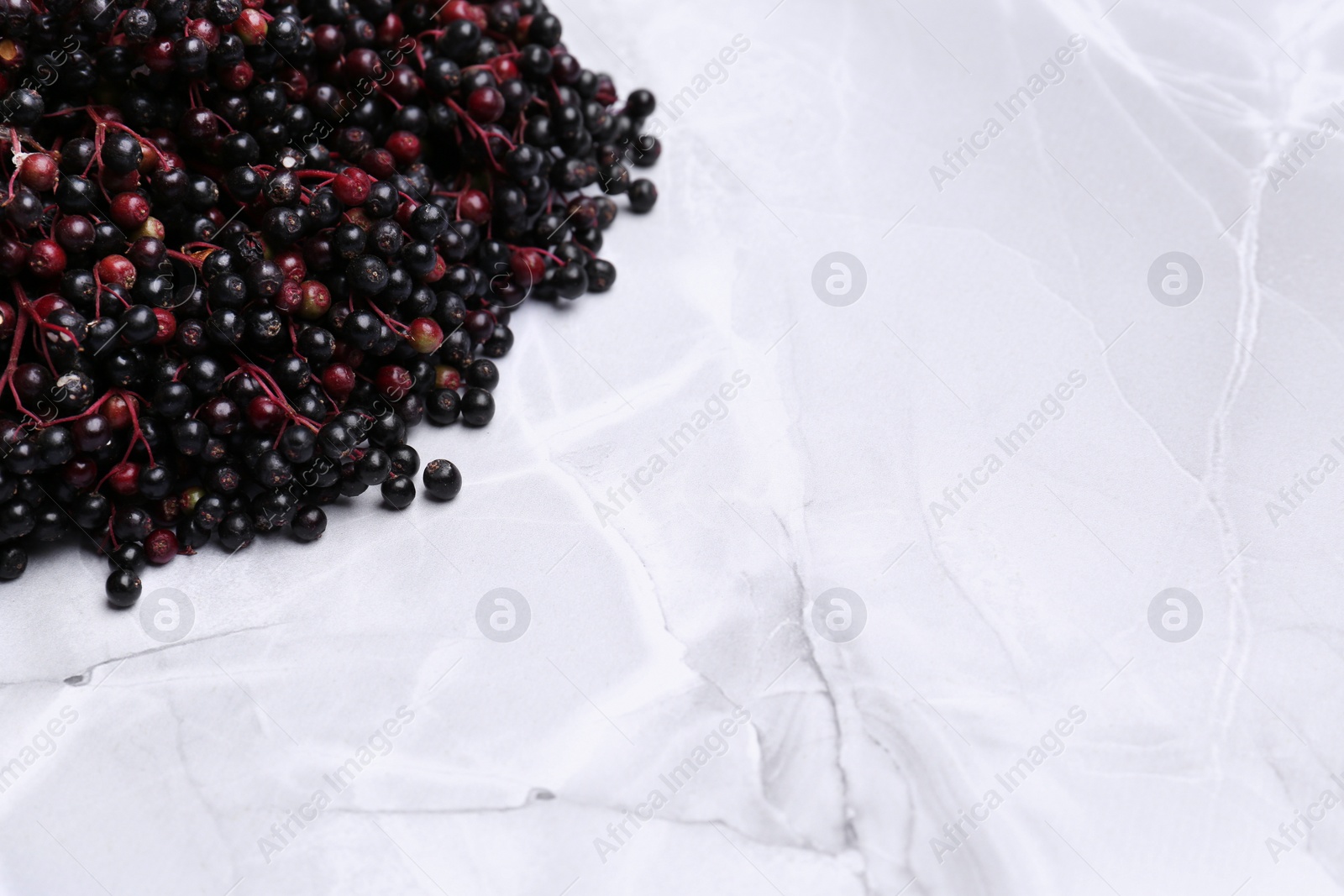 Photo of Tasty elderberries (Sambucus) on white marble table, space for text