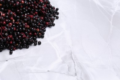 Tasty elderberries (Sambucus) on white marble table, space for text