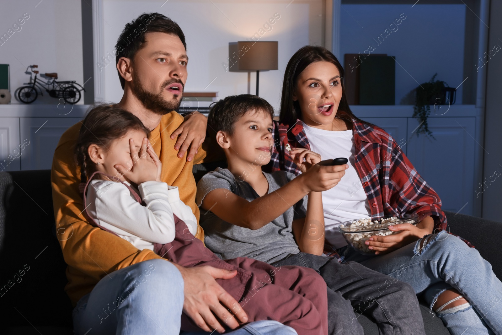 Photo of Emotional family watching TV at home in evening. Son changing channels with remote control