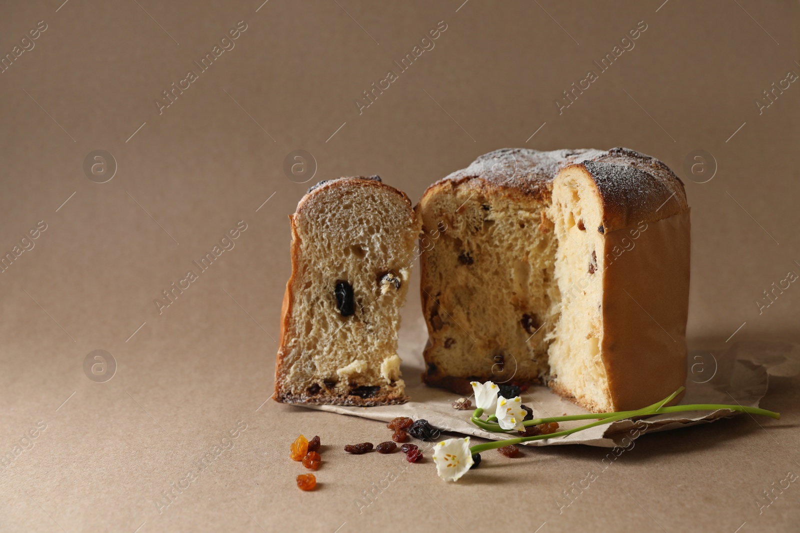 Photo of Delicious cut Panettone cake, raisins and beautiful flowers on light brown background, space for text. Traditional Italian pastry