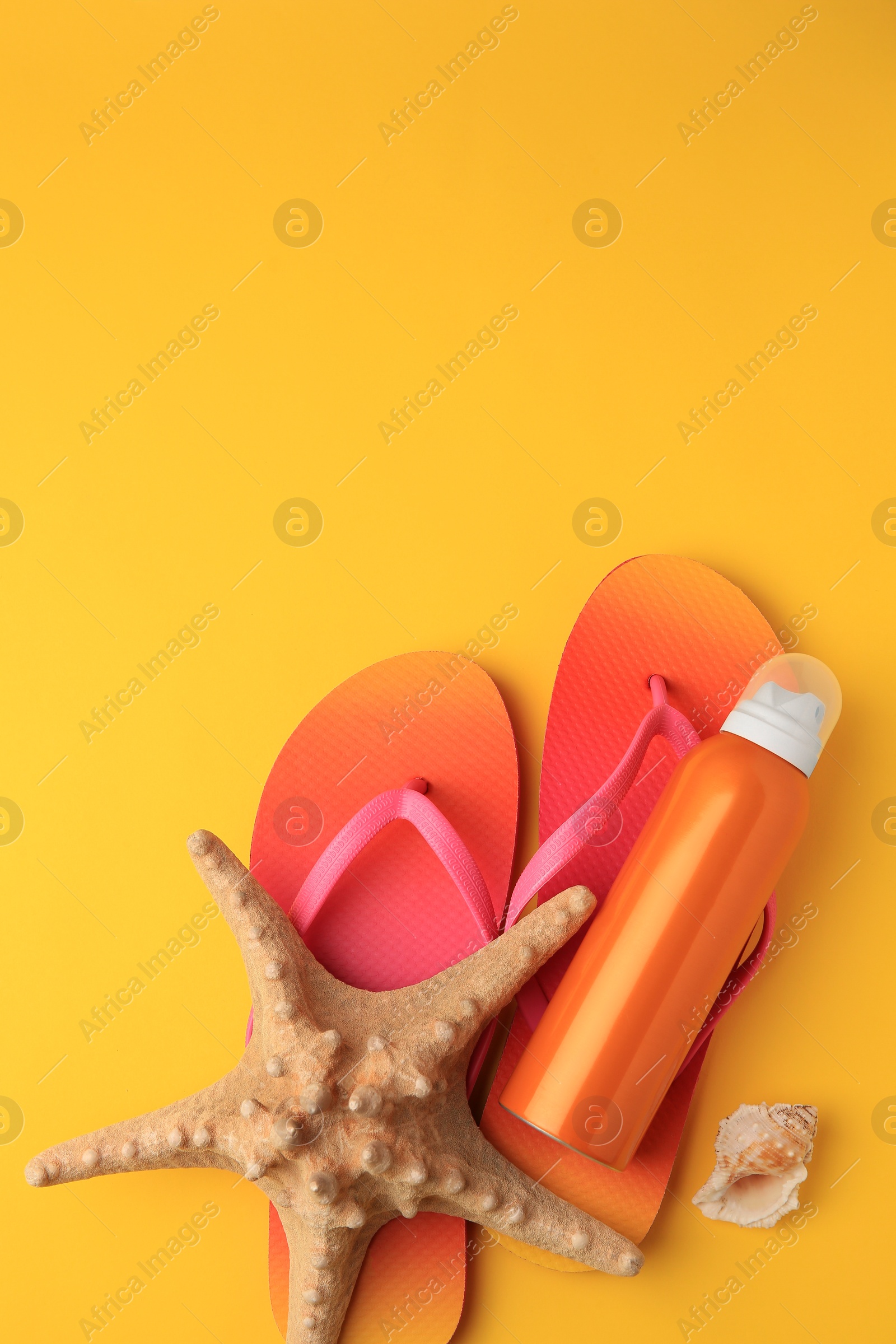 Photo of Sunscreen, starfish, shell and flip flops on orange background, flat lay with space for text. Sun protection