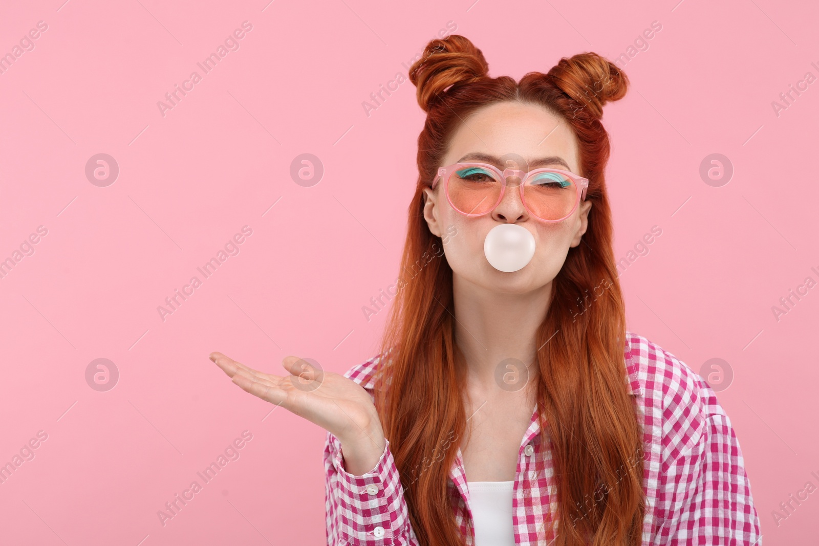 Photo of Beautiful woman with bright makeup blowing bubble gum on pink background. Space for text