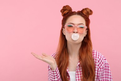 Beautiful woman with bright makeup blowing bubble gum on pink background. Space for text