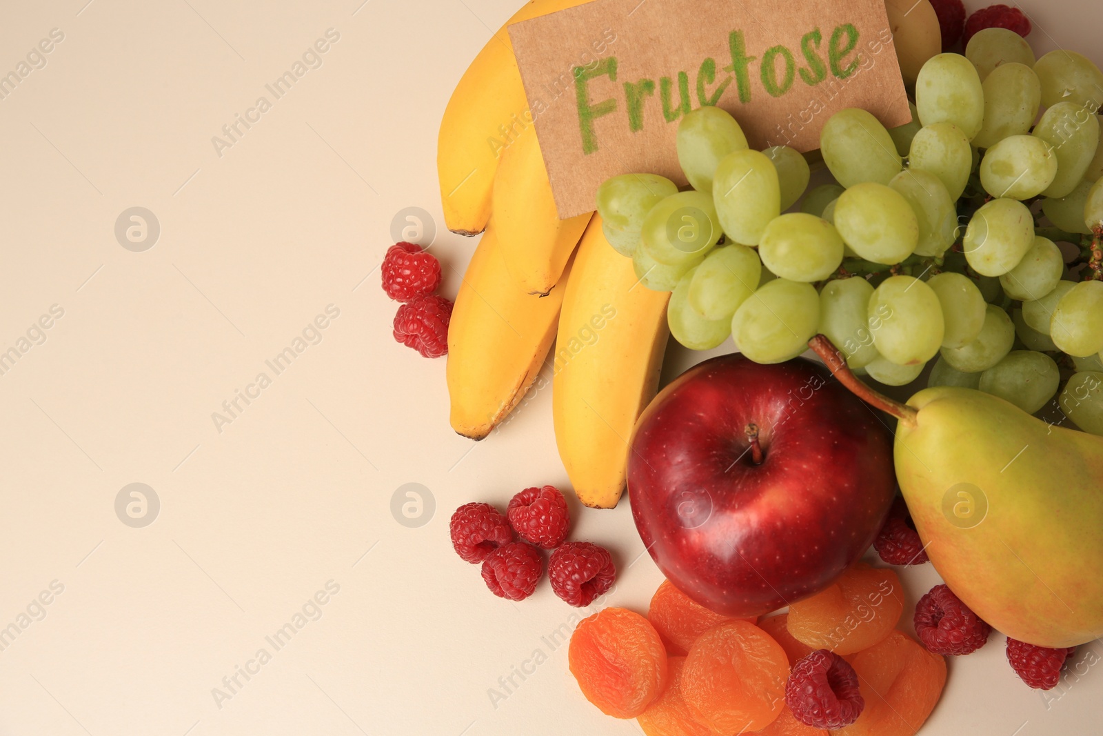 Photo of Card with word Fructose, delicious ripe fruits, raspberries and dried apricots on beige table, flat lay. Space for text