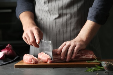 Photo of Man cutting fresh raw meat on grey table, closeup