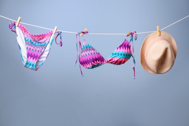 Stylish bikini and hat hanging on rope against color background