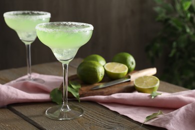 Delicious Margarita cocktail in glasses, lime and leaves on wooden table, closeup