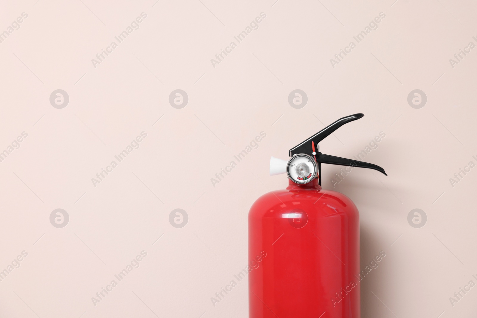 Photo of One fire extinguisher on beige wall, space for text