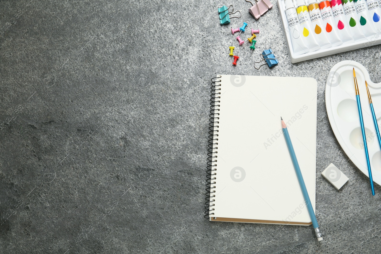 Photo of Flat lay composition with blank sketchbook on grey stone table. Space for text