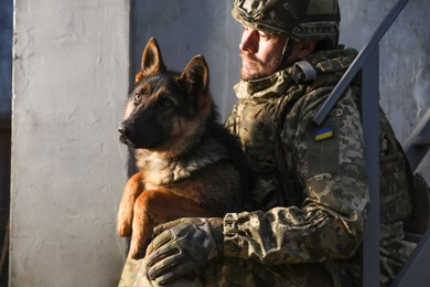 Photo of Ukrainian soldier with German shepherd dog near wall outdoors