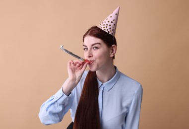 Photo of Young woman in party hat with blower on beige background