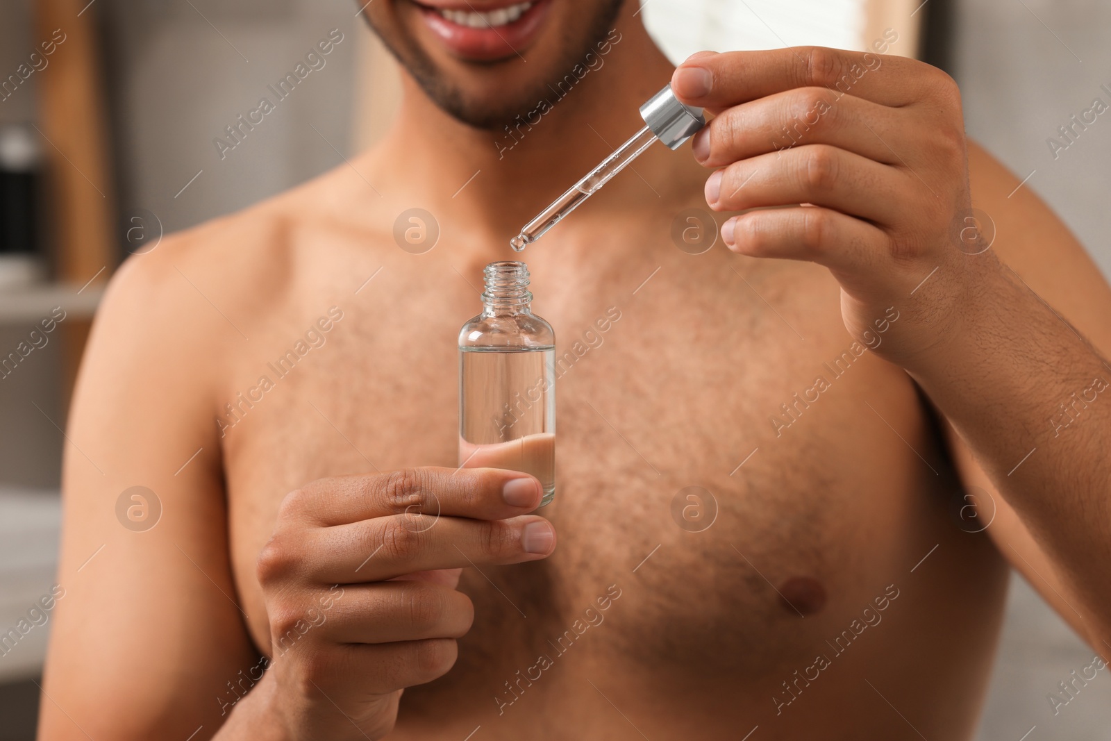 Photo of Man with cosmetic serum in hands in bathroom, closeup