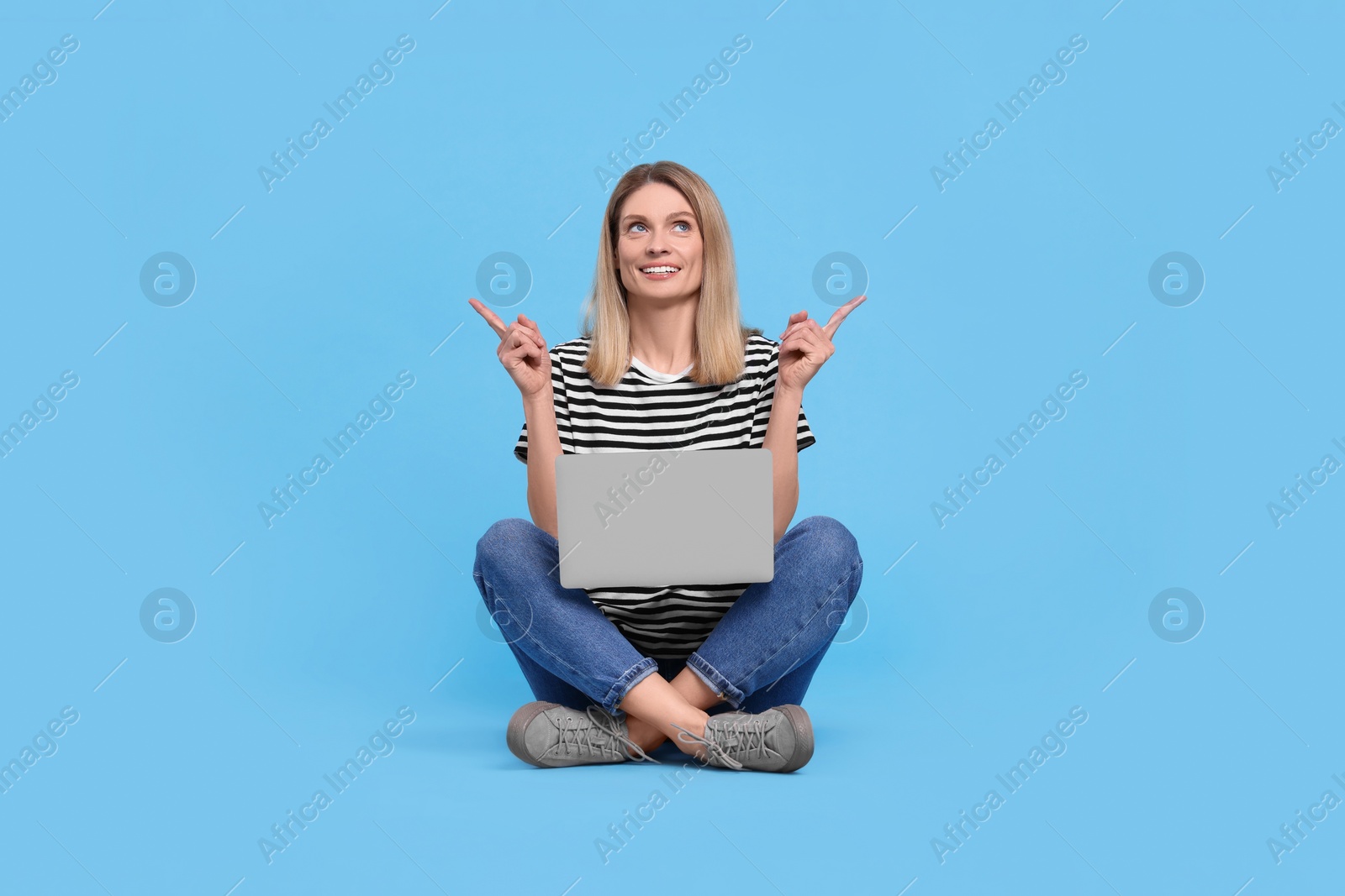 Photo of Happy woman with laptop pointing at something on light blue background