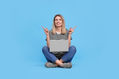 Photo of Happy woman with laptop pointing at something on light blue background