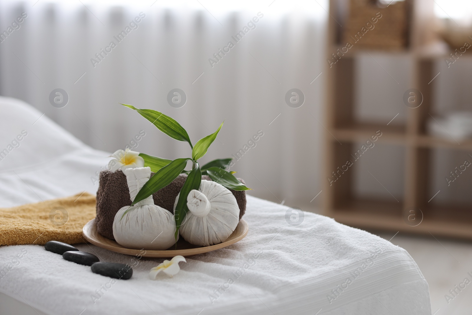 Photo of Spa stones, flowers, towel and herbal bags on massage table indoors