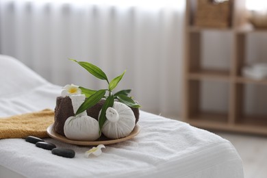 Spa stones, flowers, towel and herbal bags on massage table indoors