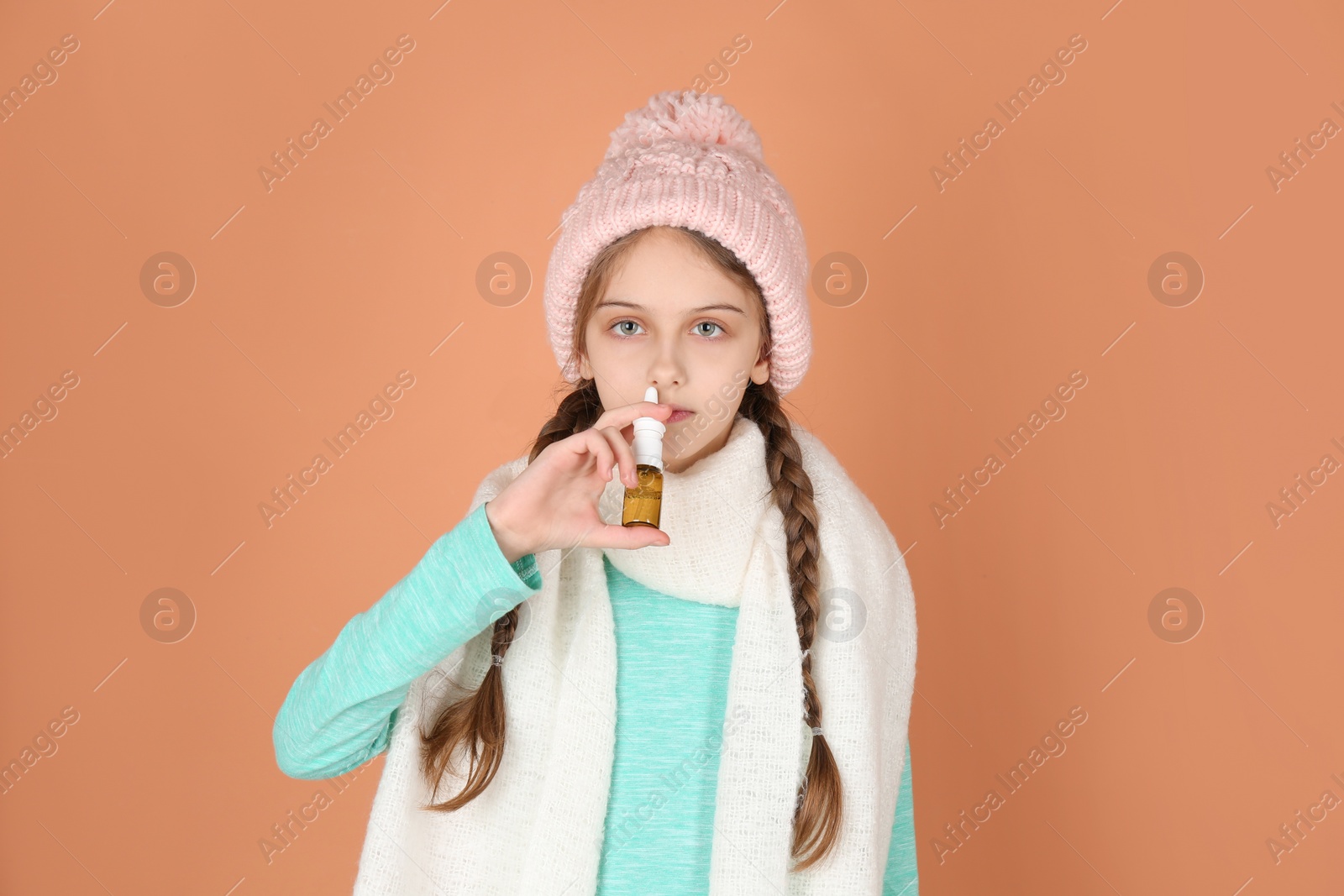 Photo of Sick little girl using nasal spray on coral background