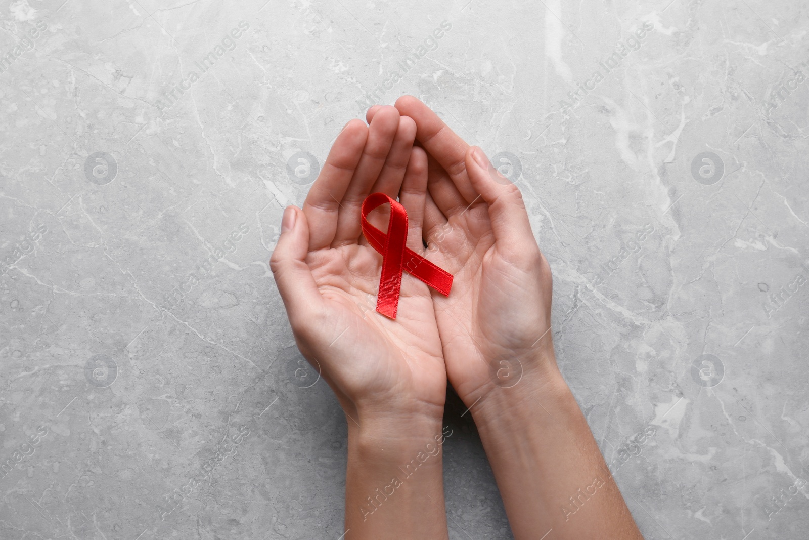 Photo of Woman holding red awareness ribbon at light grey marble table, top view. World AIDS disease day