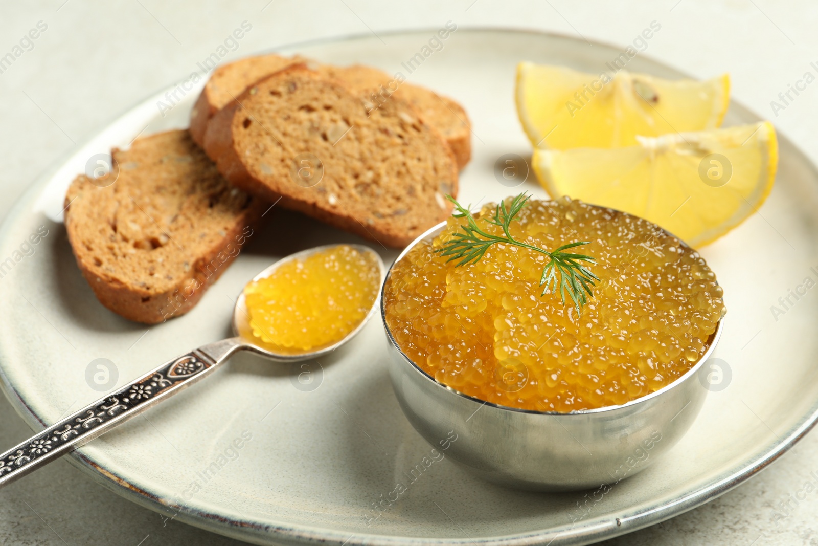 Photo of Fresh pike caviar in bowl, lemon and bread on light table, closeup