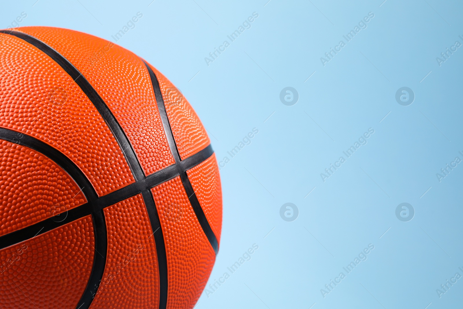 Photo of One orange basketball ball on light blue background, closeup. Space for text