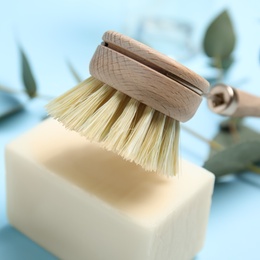 Photo of Cleaning brush and soap bar for dish washing on light blue background, closeup