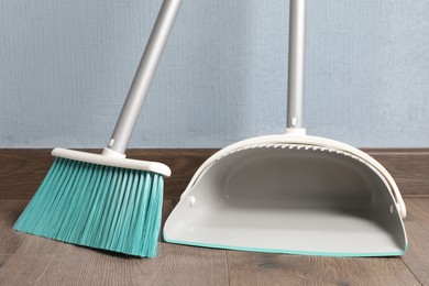 Photo of Plastic broom with dustpan near light blue wall indoors