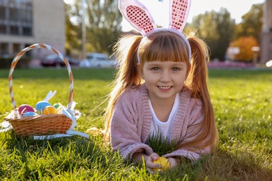 Cute little girl with bunny ears and basket of Easter eggs in park