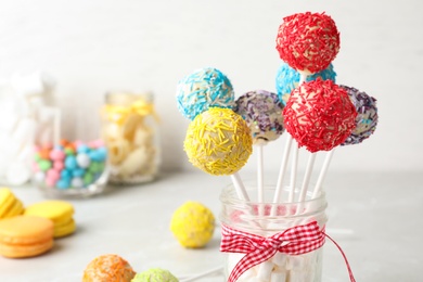 Photo of Yummy bright cake pops in glass jar full of marshmallows on table. Space for text