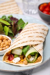 Photo of Delicious hummus wrap with vegetables on table, closeup