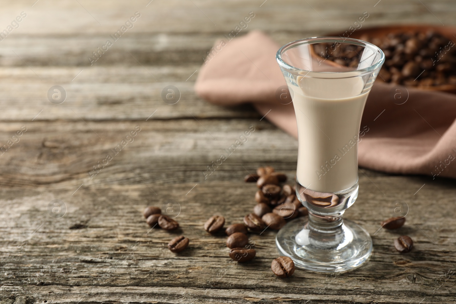 Photo of Coffee cream liqueur in glass and beans on wooden table, space for text