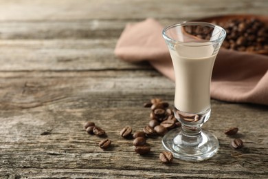 Coffee cream liqueur in glass and beans on wooden table, space for text