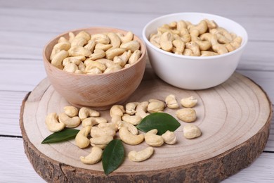 Photo of Tasty cashew nuts and green leaves on light wooden table