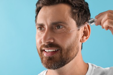 Smiling man applying cosmetic serum onto his face on light blue background