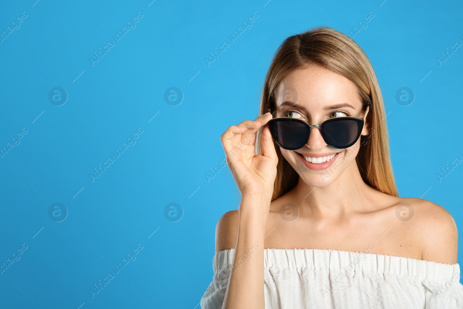 Photo of Beautiful woman in stylish sunglasses on light blue background, space for text