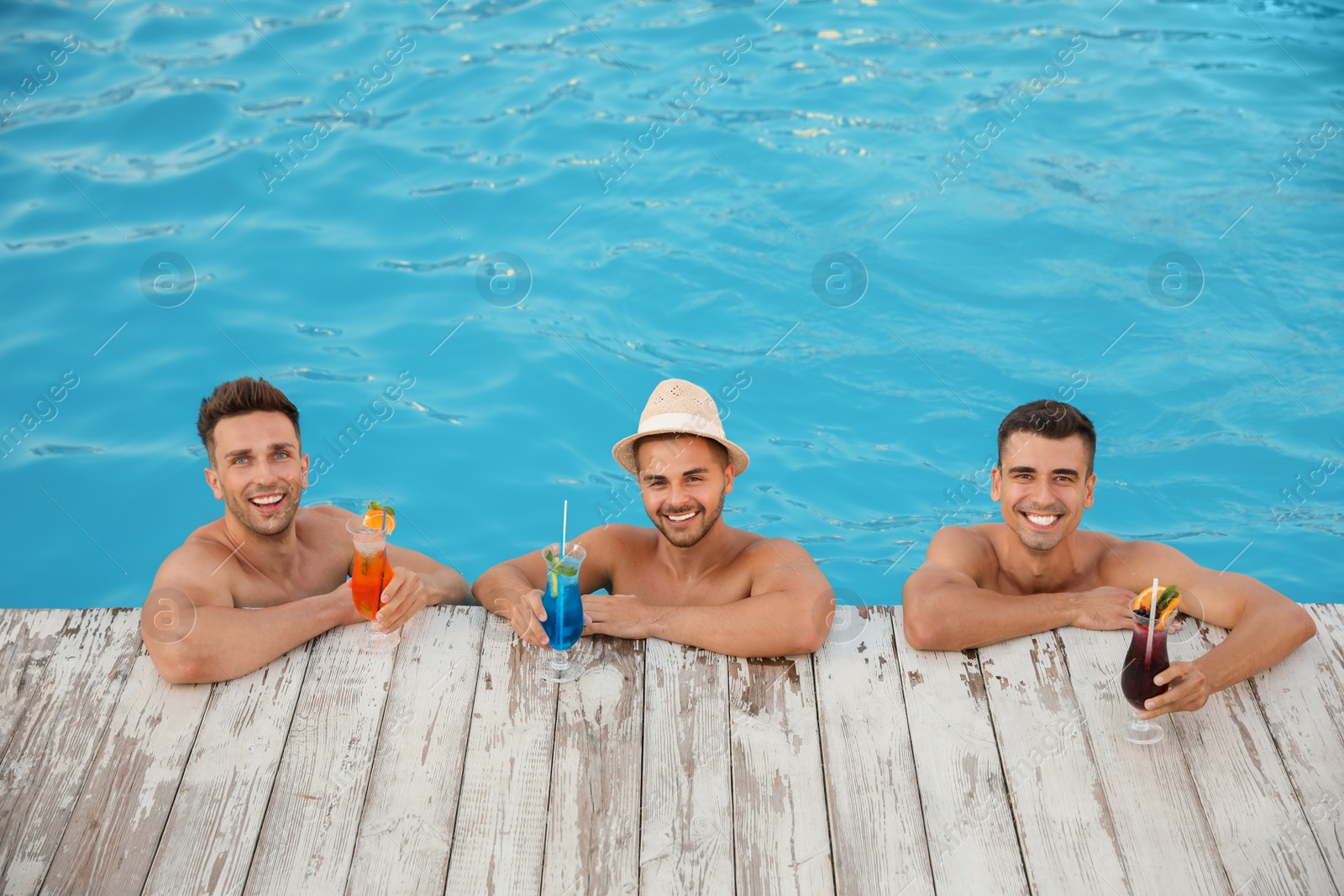 Photo of Happy young friends with refreshing cocktails in swimming pool