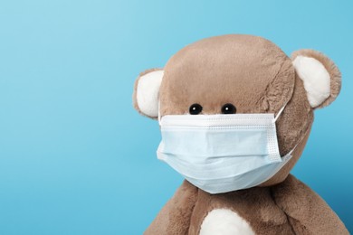 Cute teddy bear in mask on light blue background, space for text