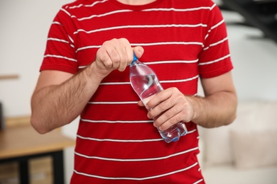 Photo of Young man with bottle of water at home, closeup