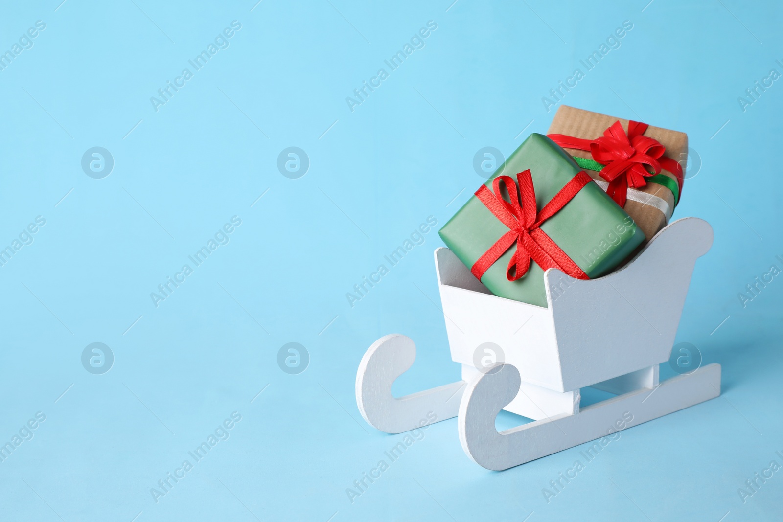 Photo of White wooden sleigh with Christmas gift boxes on light blue background, space for text