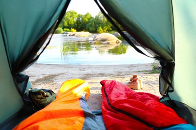 Photo of Camping tent with sleeping bags near lake, view from inside