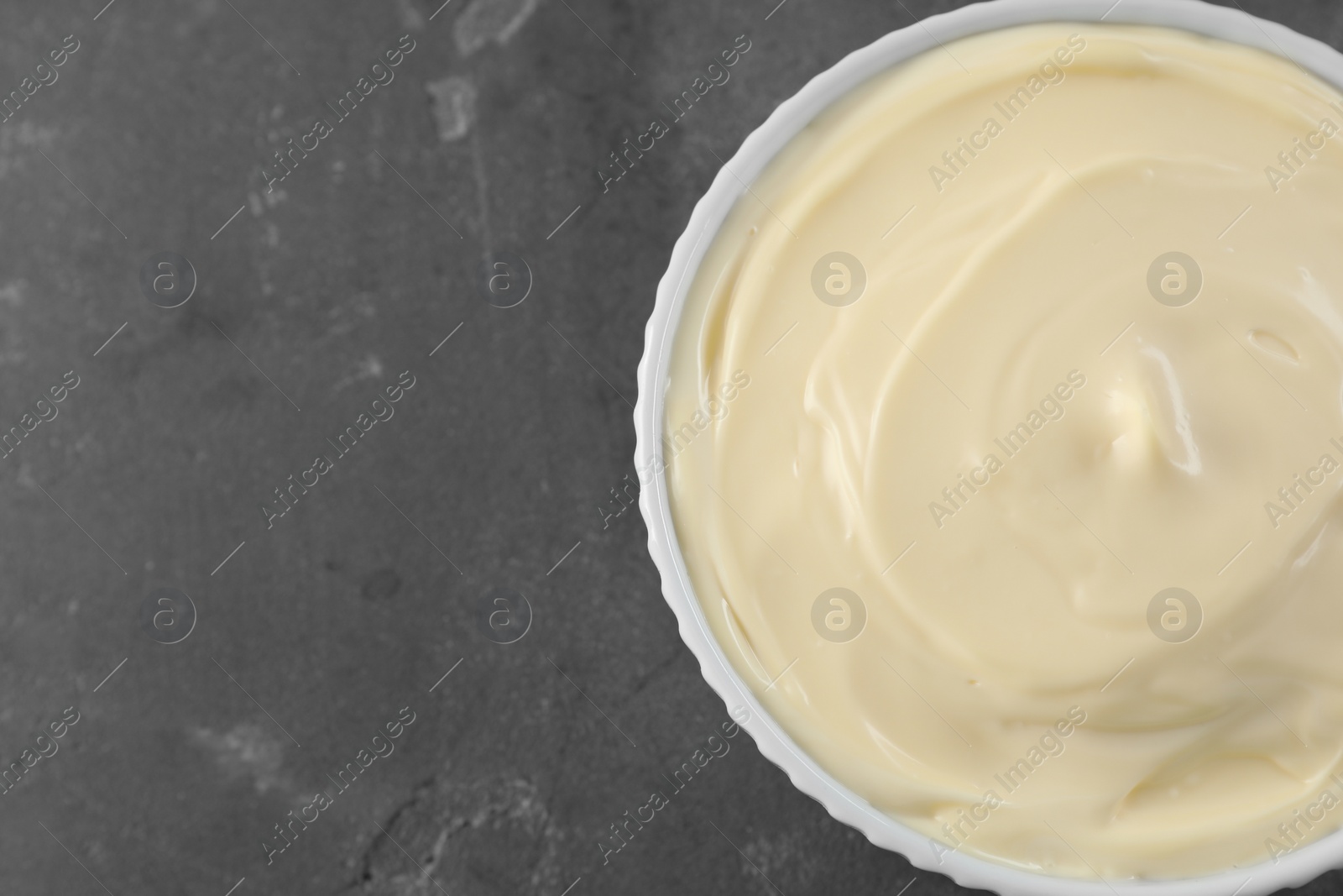 Photo of Fresh mayonnaise sauce in bowl on grey table, top view. Space for text