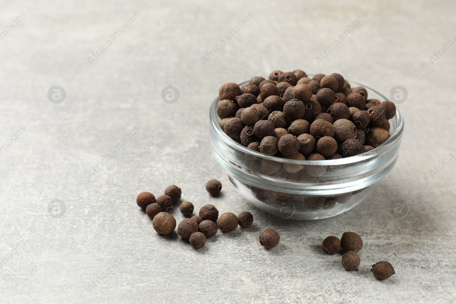 Photo of Aromatic allspice pepper grains in glass bowl on grey table, closeup. Space for text