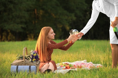 Photo of Young man giving wineglasses to his girlfriend in green park. Picnic season