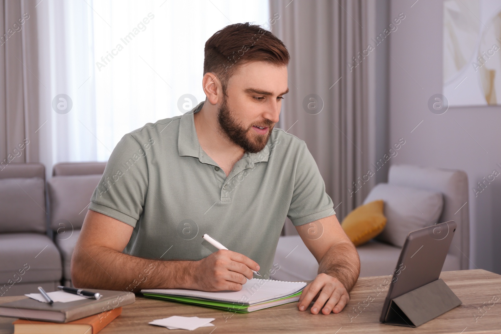 Photo of Young man taking notes during online webinar at table indoors