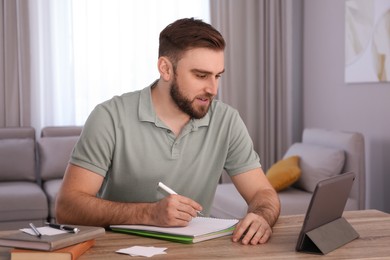 Photo of Young man taking notes during online webinar at table indoors