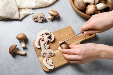 Woman cutting fresh wild mushrooms at light grey table, top view