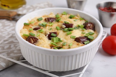 Photo of Tasty sausage casserole with green onion in baking dish on white marble table, closeup