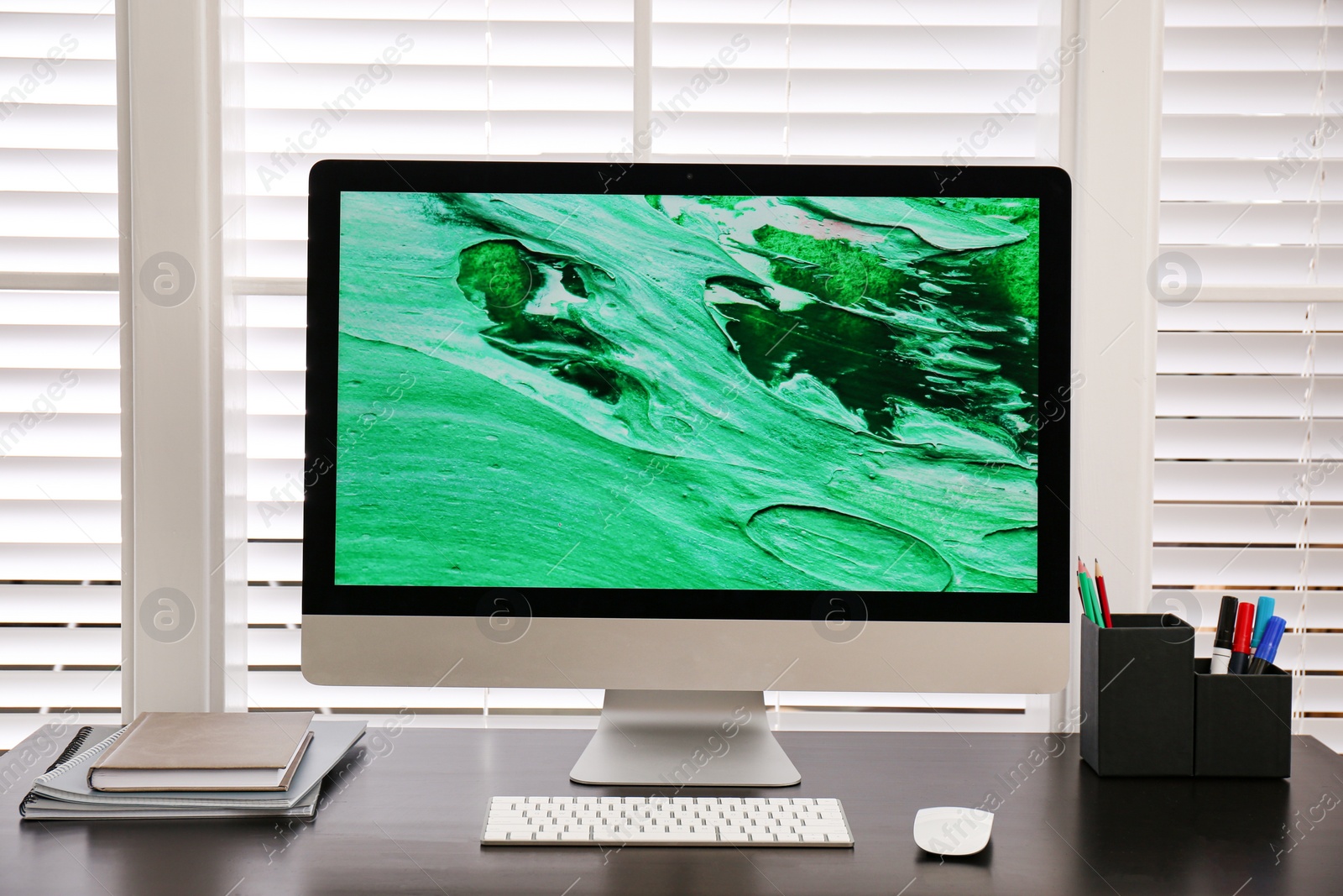 Photo of Comfortable workplace near window with white horizontal blinds in room