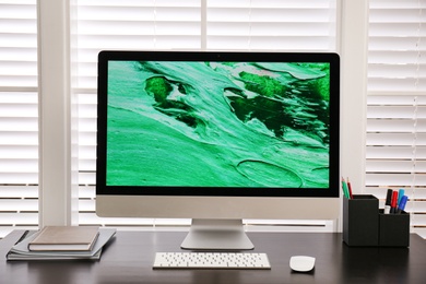 Photo of Comfortable workplace near window with white horizontal blinds in room