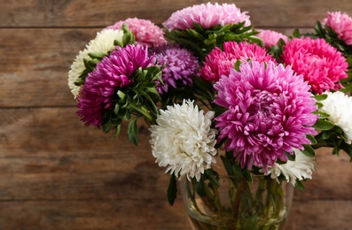 Beautiful asters in vase on wooden background. Autumn flowers